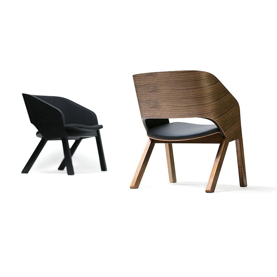 Two modern chairs on a white background, one with a bent plywood seat and black cushion, solid wood legs, the other entirely black. Both have sleek designs similar to the Armchair Merano Lounge by TON with reclined backs and angled legs.
