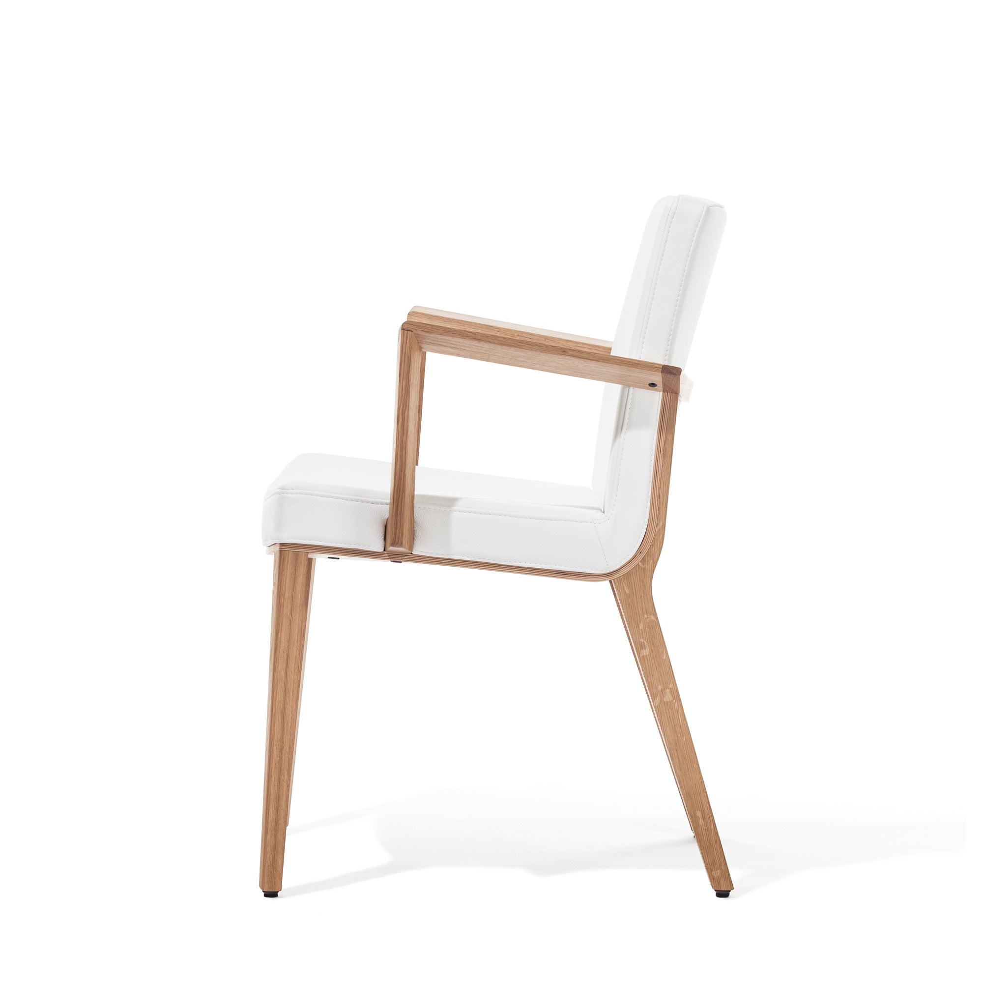The Armchair Moritz by TON, designed by Kai Stania, showcases a modern look with its wooden frame, upholstered white seat and backrest. It features angled legs and armrests which contribute to its minimalist and sleek design against a plain white background.
