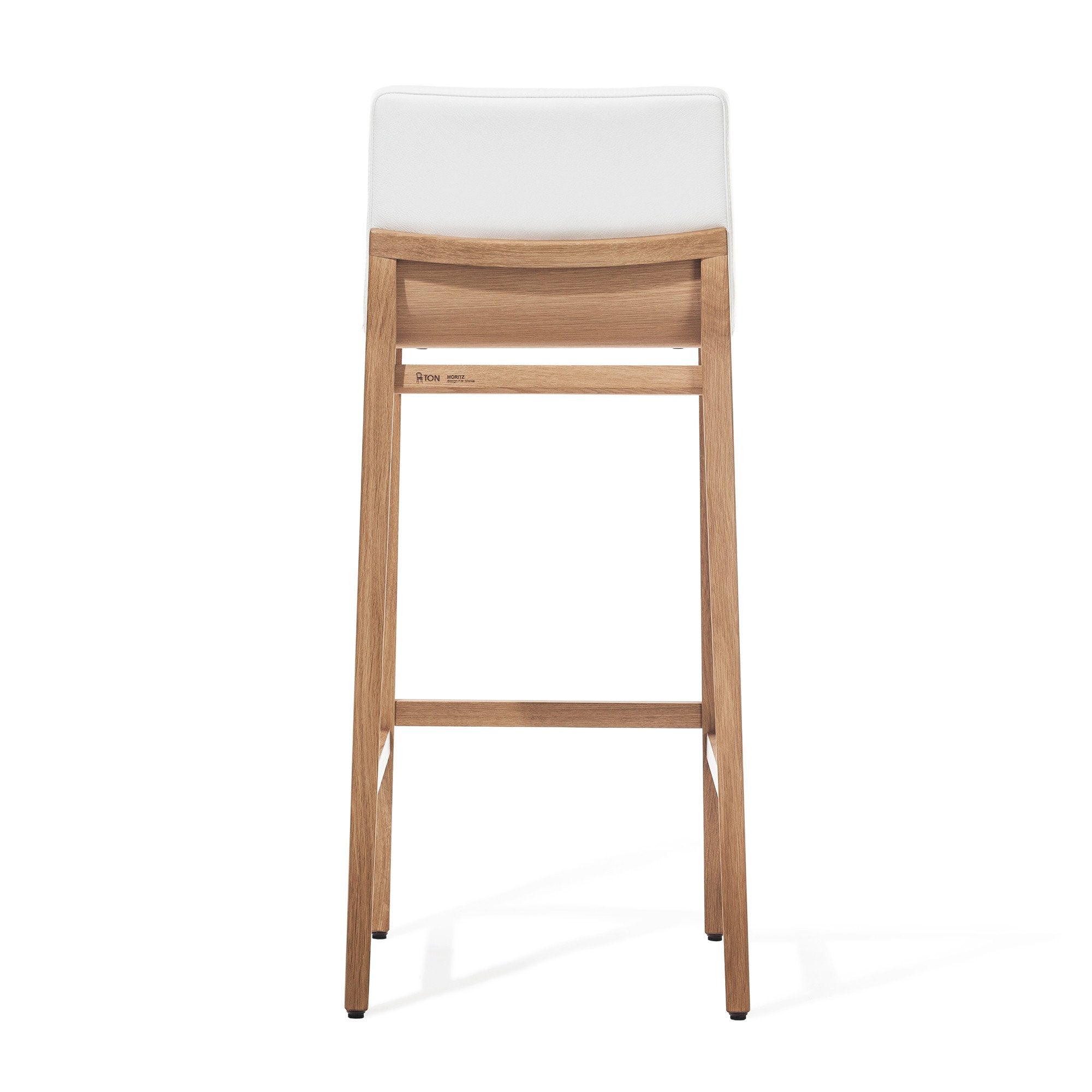 The Barstool Moritz by TONDesigner is a premium ergonomic furniture piece with a minimalist design. It features four legs, a horizontal support beam, and boasts a natural wood finish with a modern touch. The stool comes equipped with a white seat cushion and is crafted by TON.