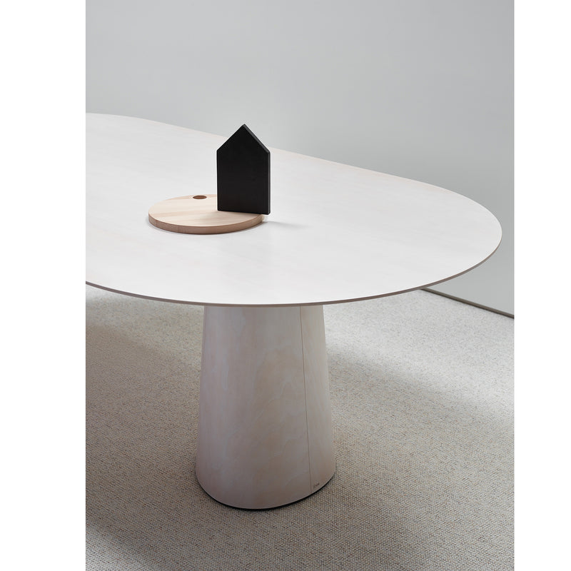 The TON P.O.V. Table 464 features a minimalist design with an oval white top and organically shaped base against a neutral backdrop. A round wooden tray with a small black house-shaped object sits on it, complemented by a light carpeted floor for warmth.