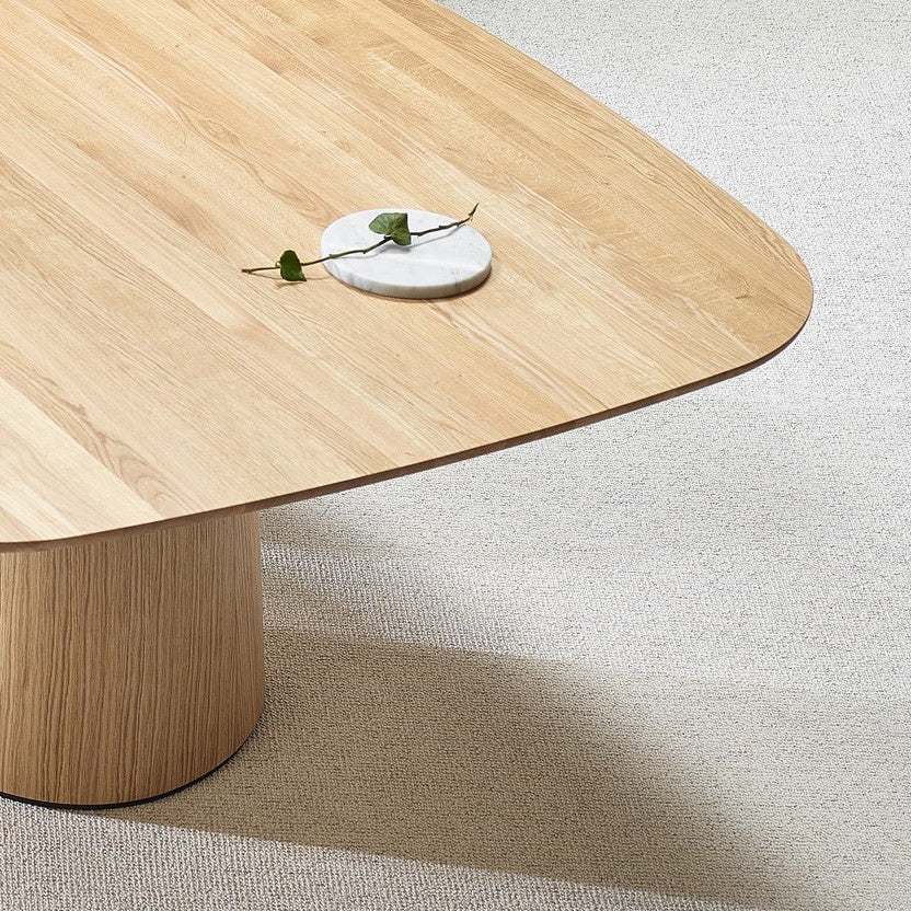 The P.O.V. Table 465 by TON, with a rounded edge and cylindrical base, showcases organic design on a textured carpet. Its solid wood surface is adorned by a small round marble dish with green leaves.