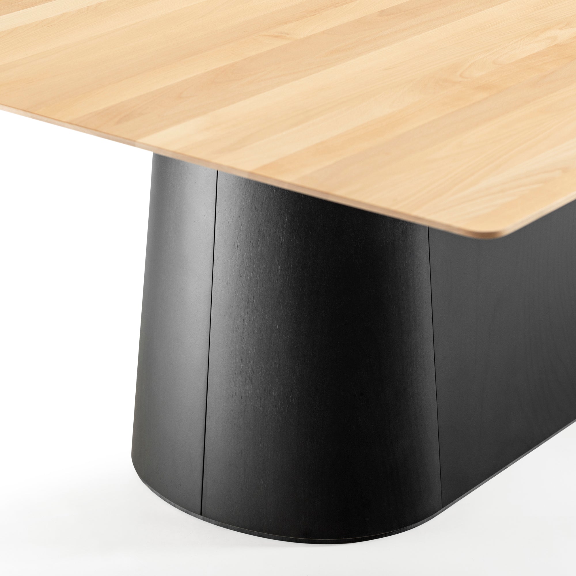 The P.O.V. Table 467 by TON showcases a modern design with a light wooden top contrasted by an organic black rectangular base. The bases slightly curved, smooth surface enhances the natural wood grain detailing of the solid wood tabletop.