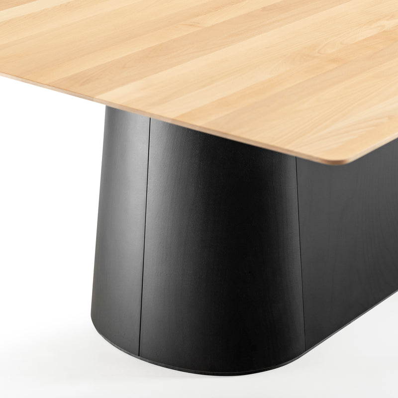 The P.O.V. Table 467 by TON showcases a modern design with a light wooden top contrasted by an organic black rectangular base. The bases slightly curved, smooth surface enhances the natural wood grain detailing of the solid wood tabletop.