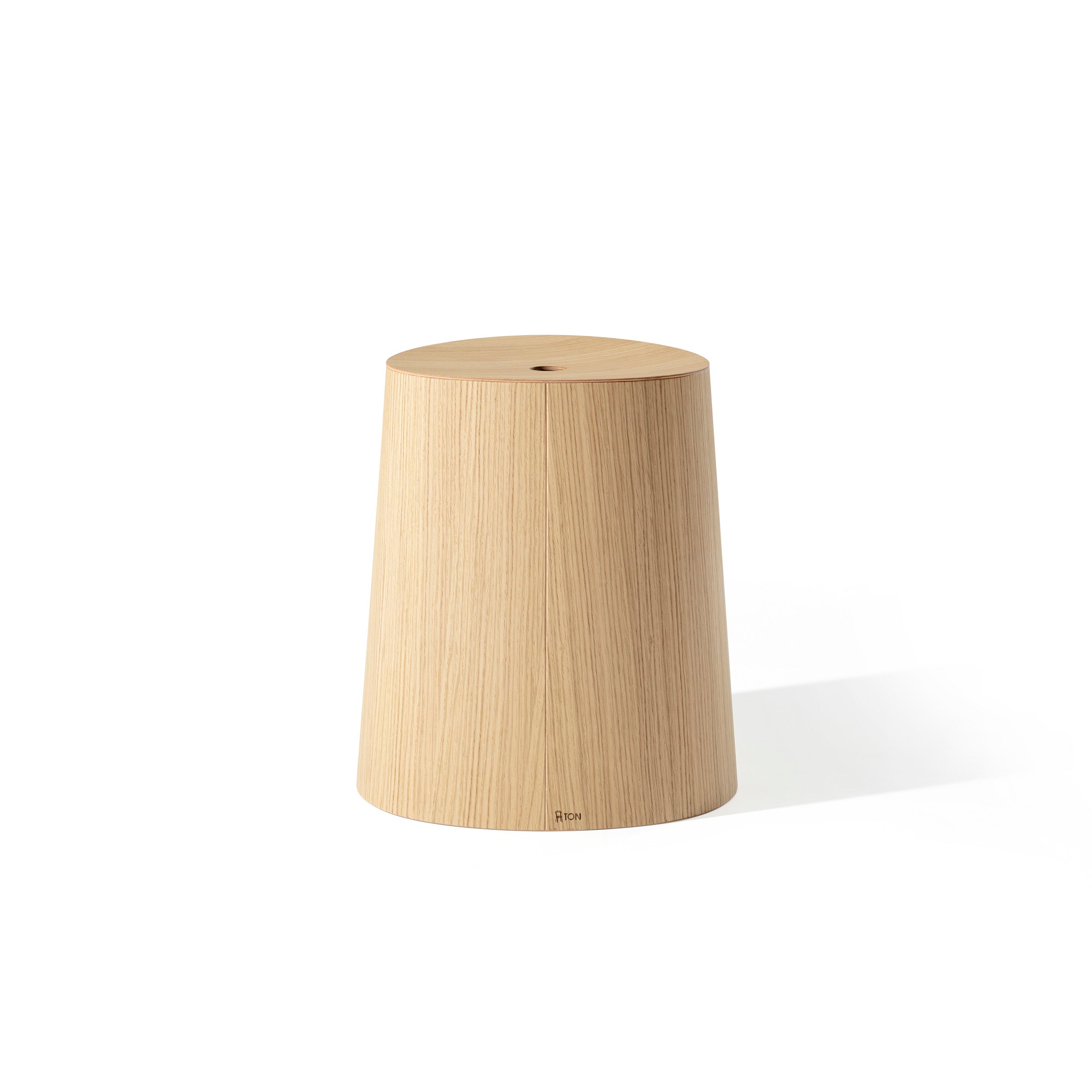 The P.O.V. Stool by TON is a cylindrical, minimalist wooden stool with a smooth finish and wider base tapering slightly at the top. It features stackable functionality for dining spaces and is available in various wood finishes, elegantly displayed on a white background.