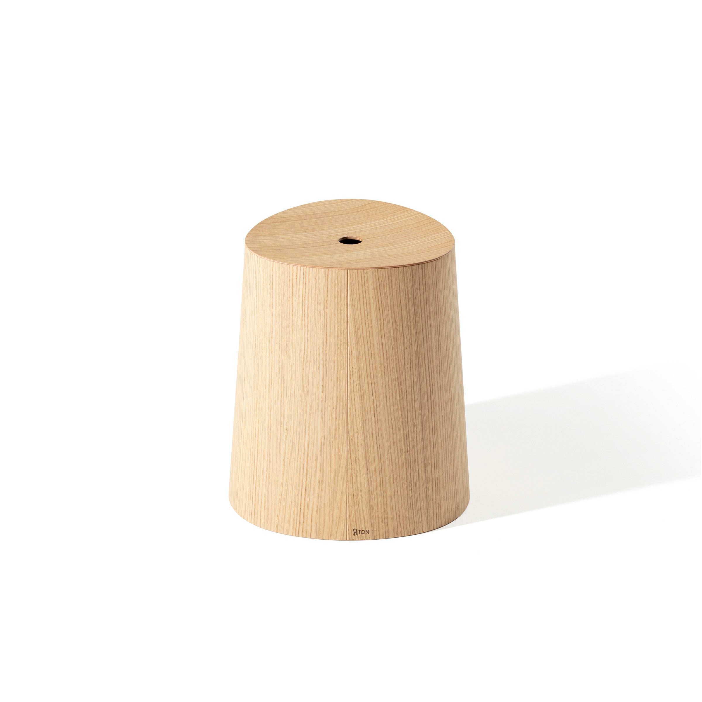 The P.O.V. Stool by TON is a designer piece with light wood and a cylindrical form, featuring a slightly flared base and a small round hole on top, casting a soft shadow on the white background.