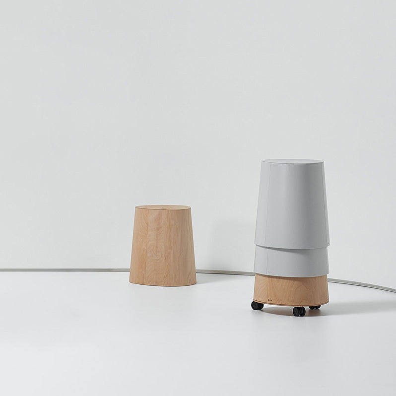 A minimalist scene features a TON P.O.V. Stool Upholstered crafted from American walnut against a plain white backdrop. Beside it, a stackable dining stool is cleverly balanced on a wooden stool with wheels, creating an intriguing composition.