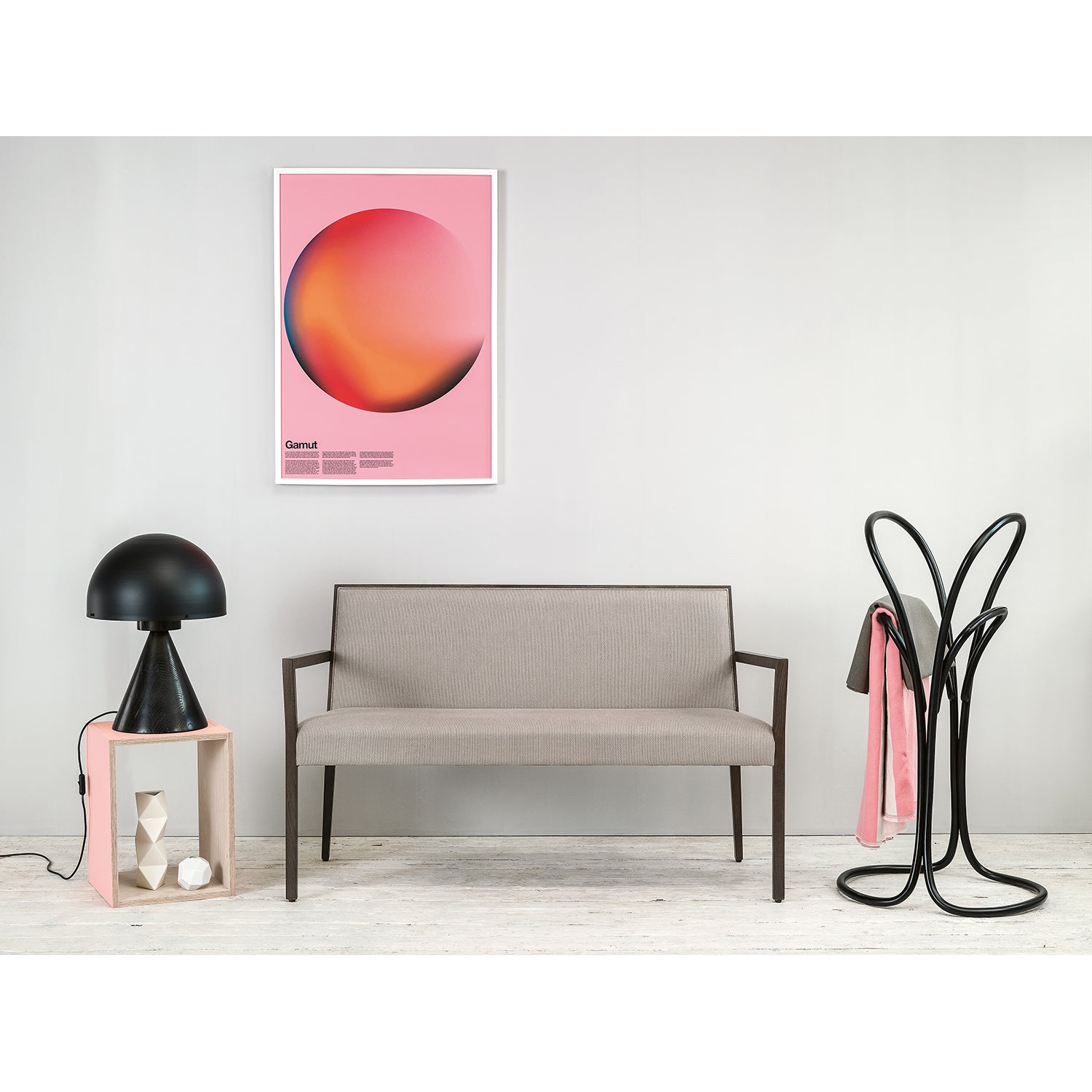 A modern interior features a gray bench, a pink side table with a black lamp, and a unique black coat rack draped with pink fabric. The PETALO abstract poster from TON adds flair with its circle designs, and the light wooden floor enhances contrast.