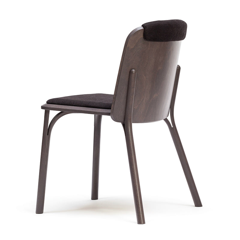 The Chair Split - Upholstered by TON features a contemporary design with a curved wooden back crafted from manually bent wood, and it boasts a black cushioned seat and backrest with sleek angled legs against a plain white background for minimalist appeal.