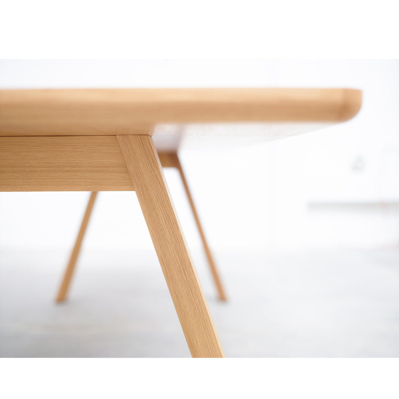 Close-up of the minimalist Table Stelvio by TON highlighting its timeless design, with a focus on the legs and tabletop edge. The light-colored wood surface and legs stand out against a softly blurred white background.