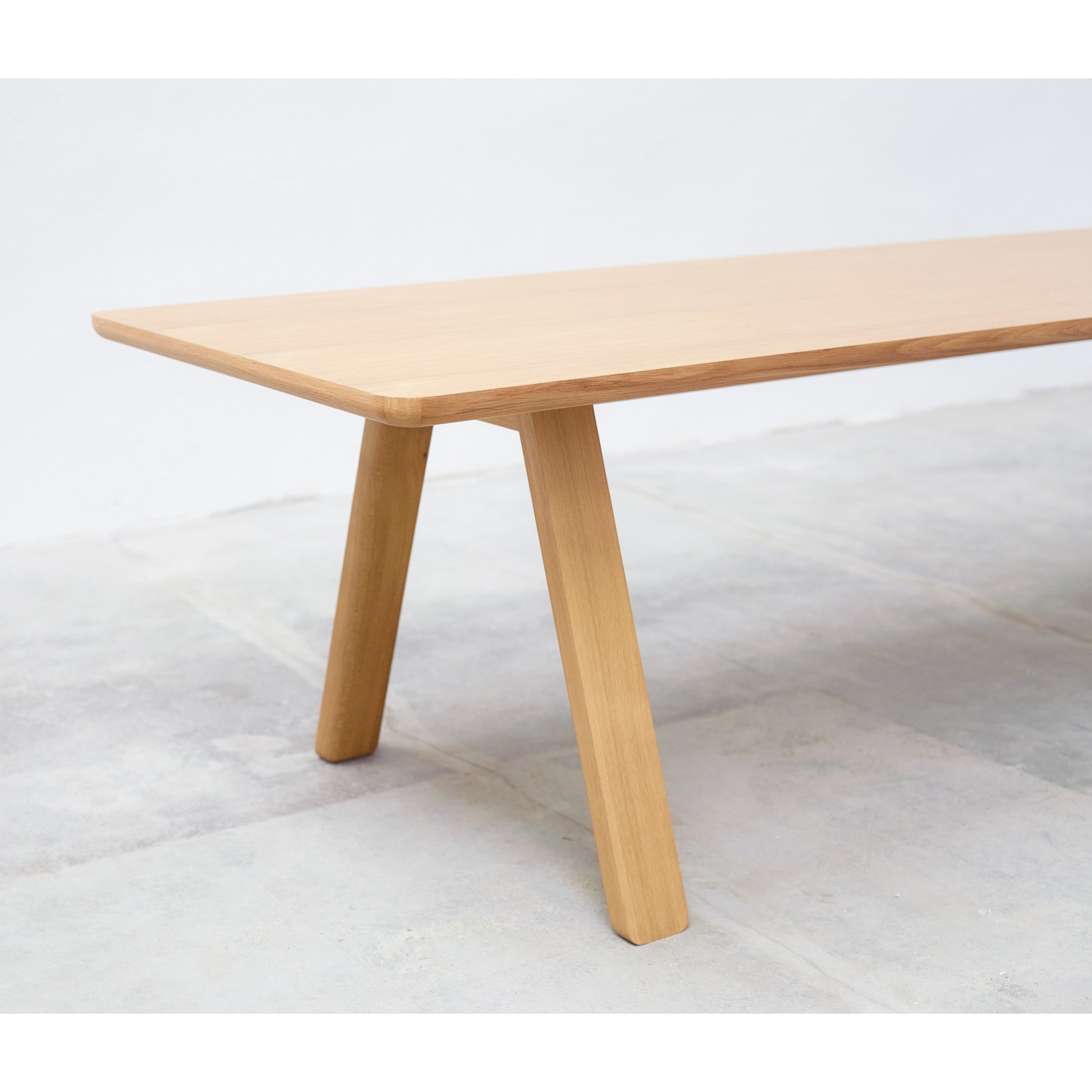 The Table Stelvio by TON features a wooden rectangular design with angled legs, set on a light gray tiled floor. Its solid wood build boasts a smooth, natural finish and embodies a timeless, minimalist style.