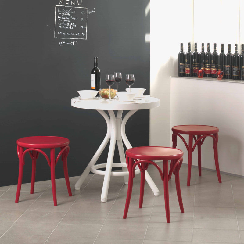 The room features a white round table with three TON Stool 60s, each with red upholstered seats. The table holds two wine glasses, a wine bottle, and a dish of apples. A chalkboard menu decorates the wall, and a row of wine bottles lines the beech wood side counter.