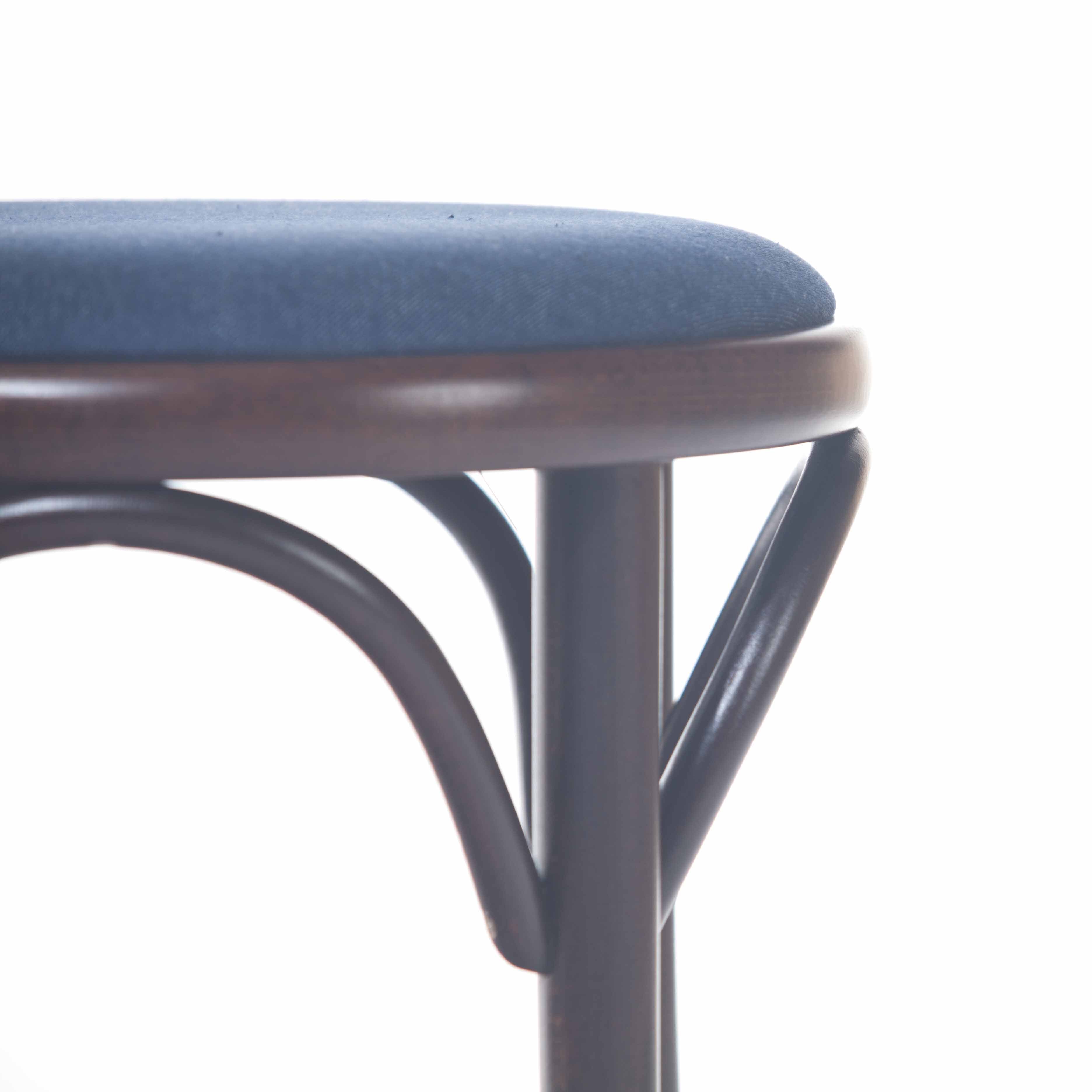 The image features the TON Stool 60 Upholstered with a blue cushioned seat and dark beech wood legs, showcasing part of its frame with curved wooden supports against a white backdrop.
