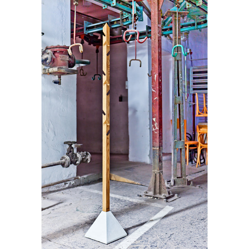 In an industrial setting with metal pipes and colorful structures, the Tee coat hanger by TON stands out with its minimalist multi-level design, crafted from oak and featuring a geometric concrete base.