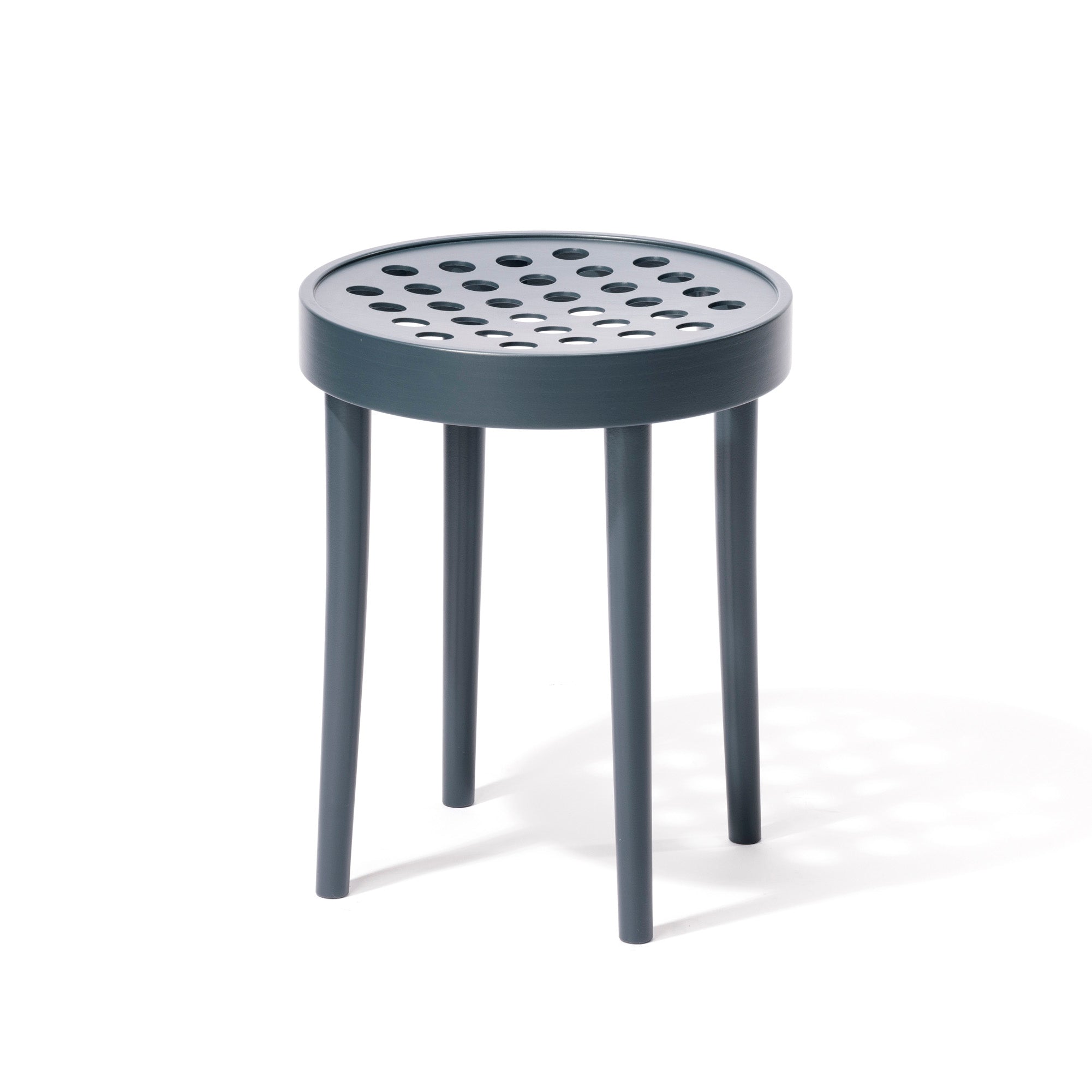 The Stool 822 by TON exemplifies Scandinavian minimalism with its round, perforated seat featuring evenly spaced holes, four slender, slightly tapered legs, and a matte dark blue-grey finish inspired by Claesson Koivisto Runes elegant designs.