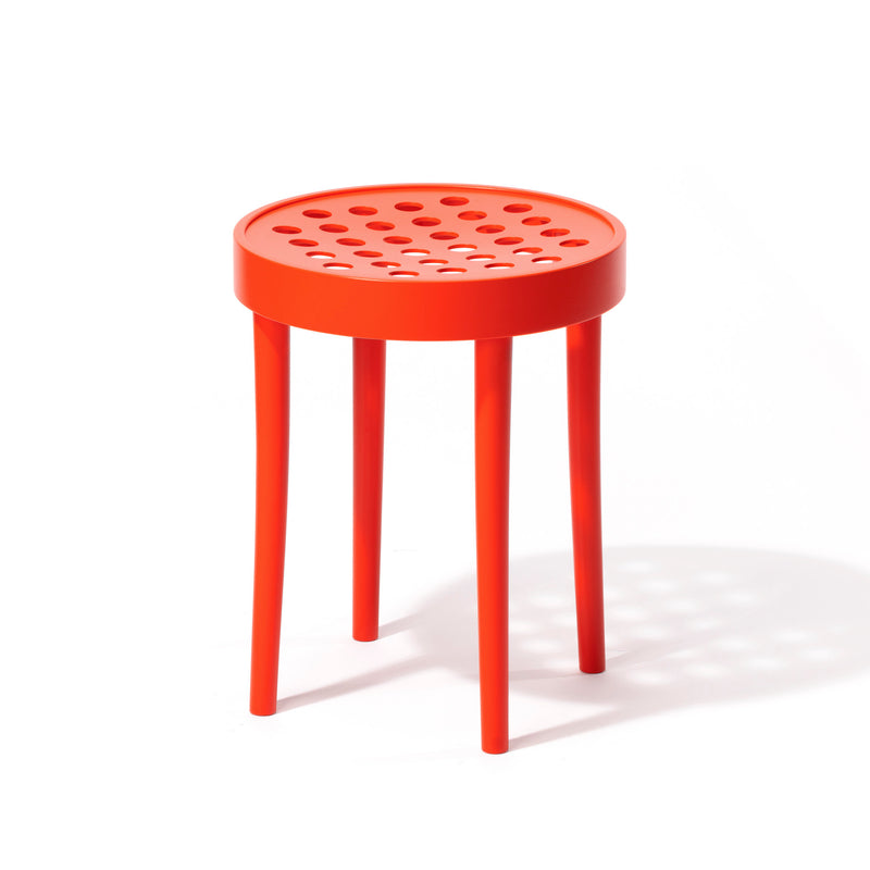 The TON Stool 822, by Claesson Koivisto Rune, showcases Scandinavian minimalism with its vibrant orange round seat and circular cutouts. It stands elegantly on three slender legs, casting a shadow on the white surface below.