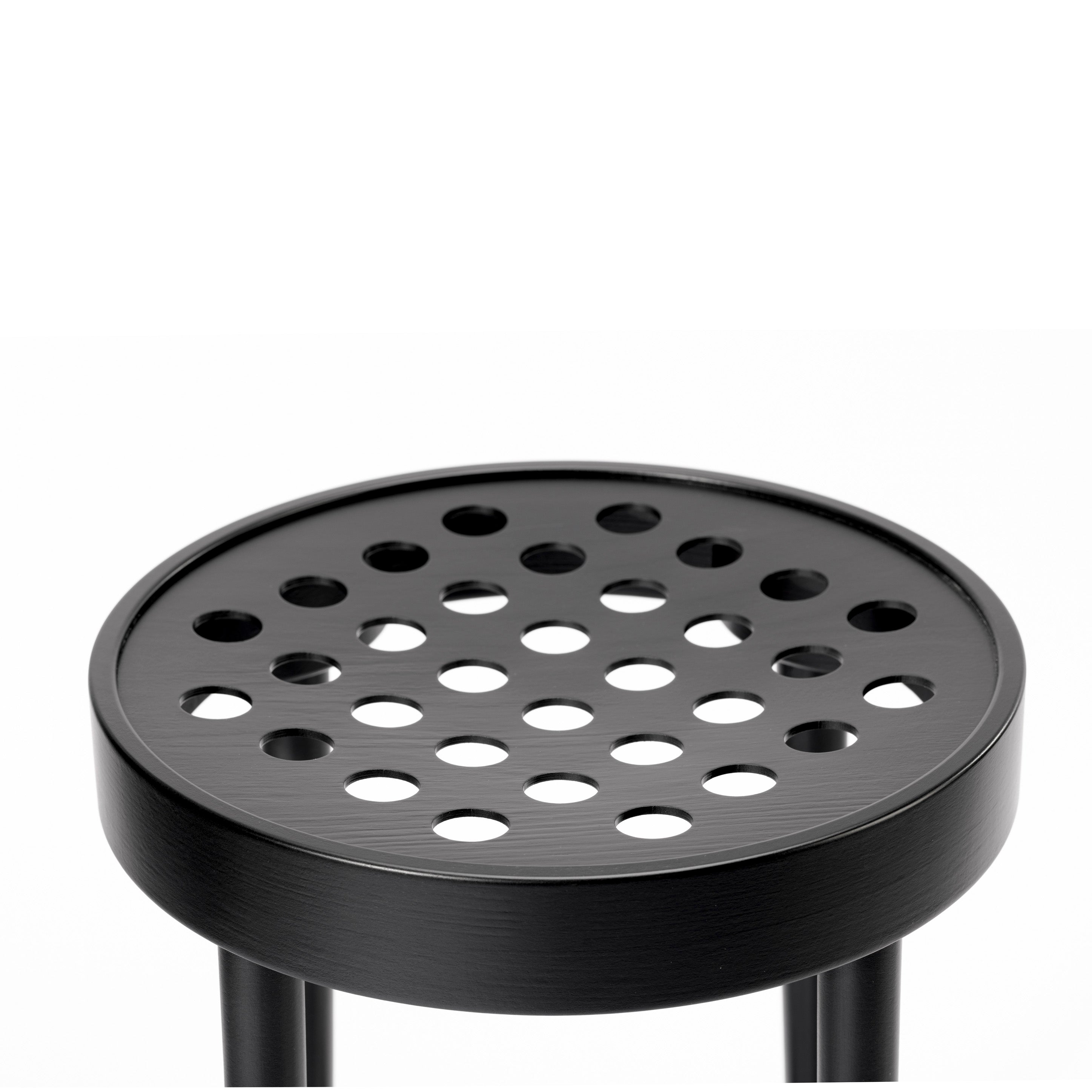 A close-up of the TON Barstool 822 showcases its black round seat with circular perforations, epitomizing Scandinavian minimalism and reflecting Claesson Koivisto Rune’s sleek, modern design aesthetic.