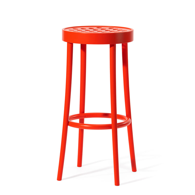 The Barstool 822 by TON features a bright red, round perforated seat with four slender legs, complemented by a circular footrest halfway down. Its design embodies Scandinavian minimalism, radiating modern elegance and simplicity.