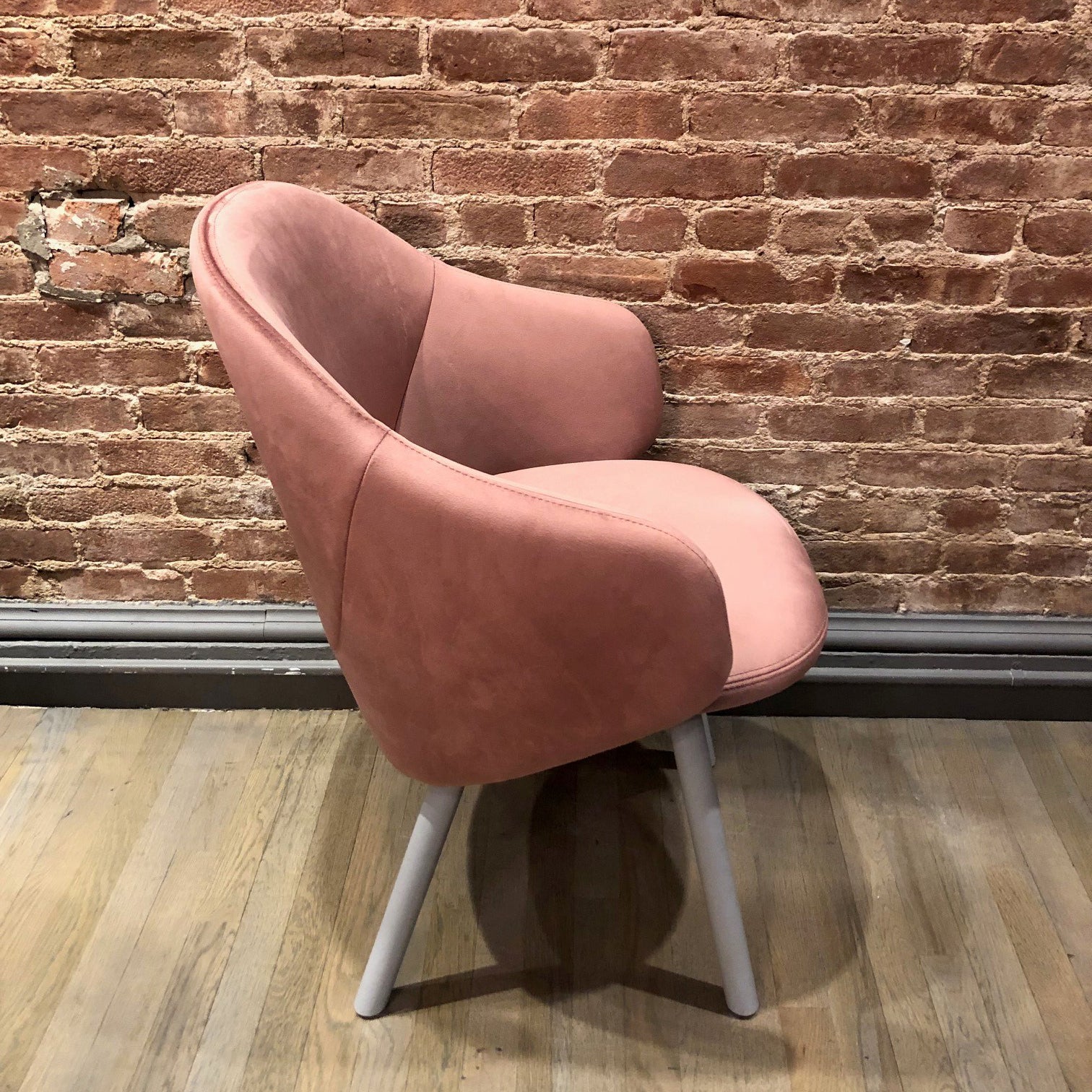 The Armchair Albu - Sale by TON features a pink, ergonomically designed upholstered seat with a rounded back. It rests on light gray legs that elegantly contrast with the textured brick wall and the hardwood floor.
