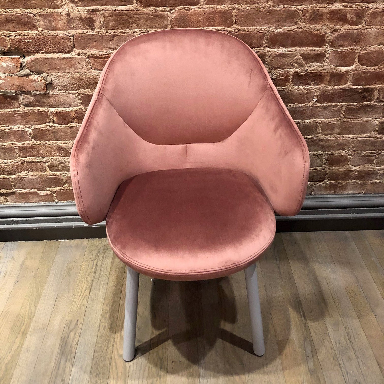 The Armchair Albu by TON, on sale, is a plush, pink velvet ergonomic chair with a curved backrest and light-colored legs. Its modern design complements the textured brick wall and wooden floor, offering high-quality upholstery for elegance and comfort.