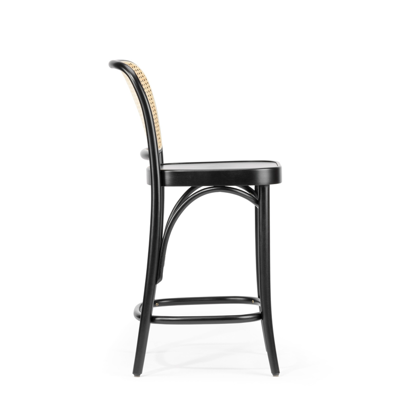 The Barstool 811 by TON is viewed from the side, showcasing black bent beech wood and a woven rattan backrest. Its sleek, curved design and footrest stand out against a plain white background.