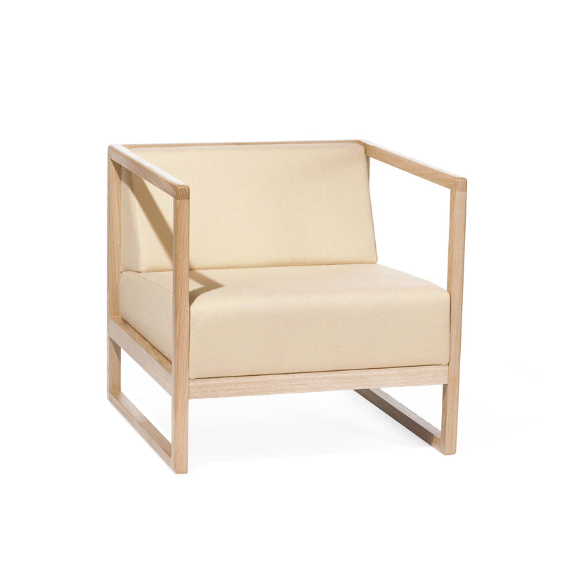 The Armchair Casablanca by TON is a beige lounge chair with a minimalistic design, featuring a square wooden frame, open sides, and cane weave armrests. It has a cushioned seat and backrest with natural wood finish contrasting the light fabric.