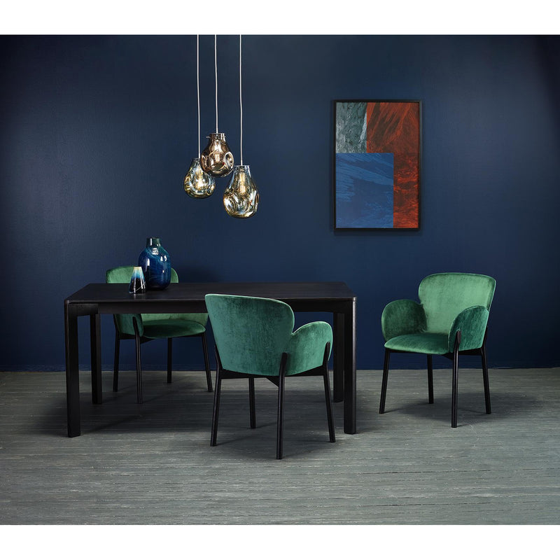 A dining room showcases modern design, featuring a sleek black table adorned with a blue vase and three green upholstered Armchair Ginger by TON on wooden flooring. Three pendant lights hang overhead, while a colorful abstract painting decorates the dark blue wall.