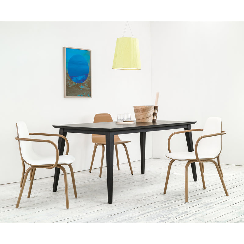 A modern dining room showcases a Jylland Table by TON, characterized by its sleek black extendable design. Four chairs with light wood frames and white cushions complement the table. A blue abstract painting adorns the wall, while a beige pendant lamp hovers above. The floor features white wooden planks in Scandinavian style.