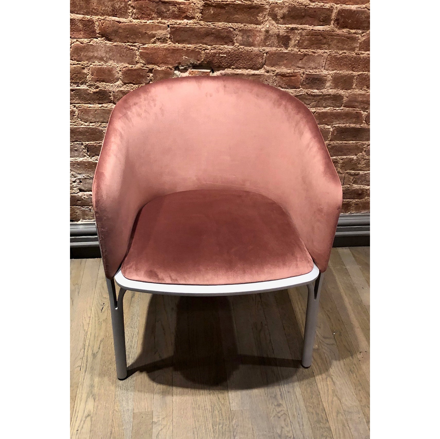 The Armchair Split - Sale by TON, featuring a pink velvet seat with a rounded back and metallic legs, is ergonomically set against a textured brick wall on a wooden floor.