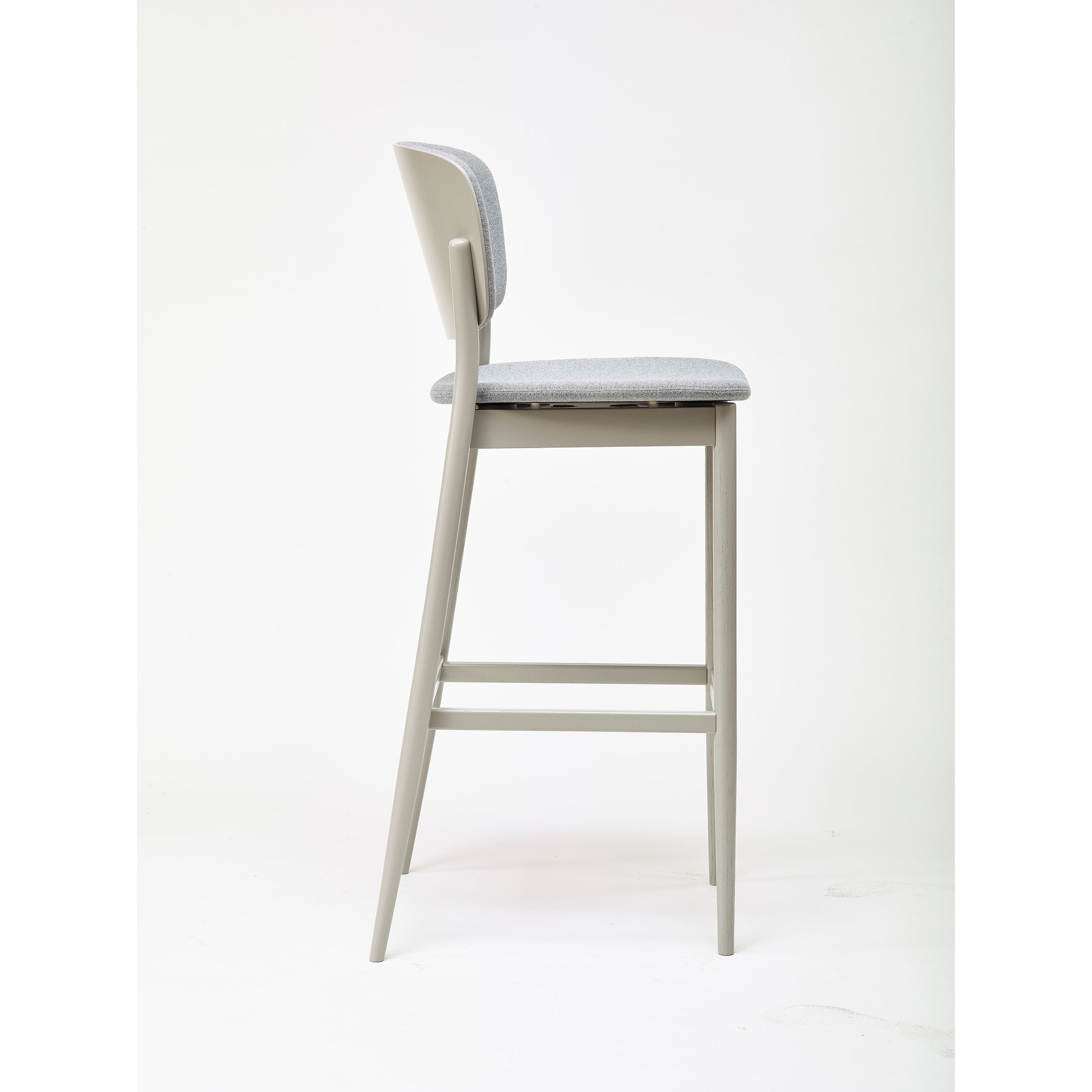 The Barstool Valencia by TON boasts a modern, sleek design with a light gray cushioned seat and backrest. Designed by Yonoh, it features minimalist, slim, light-colored wooden legs against a plain white background.