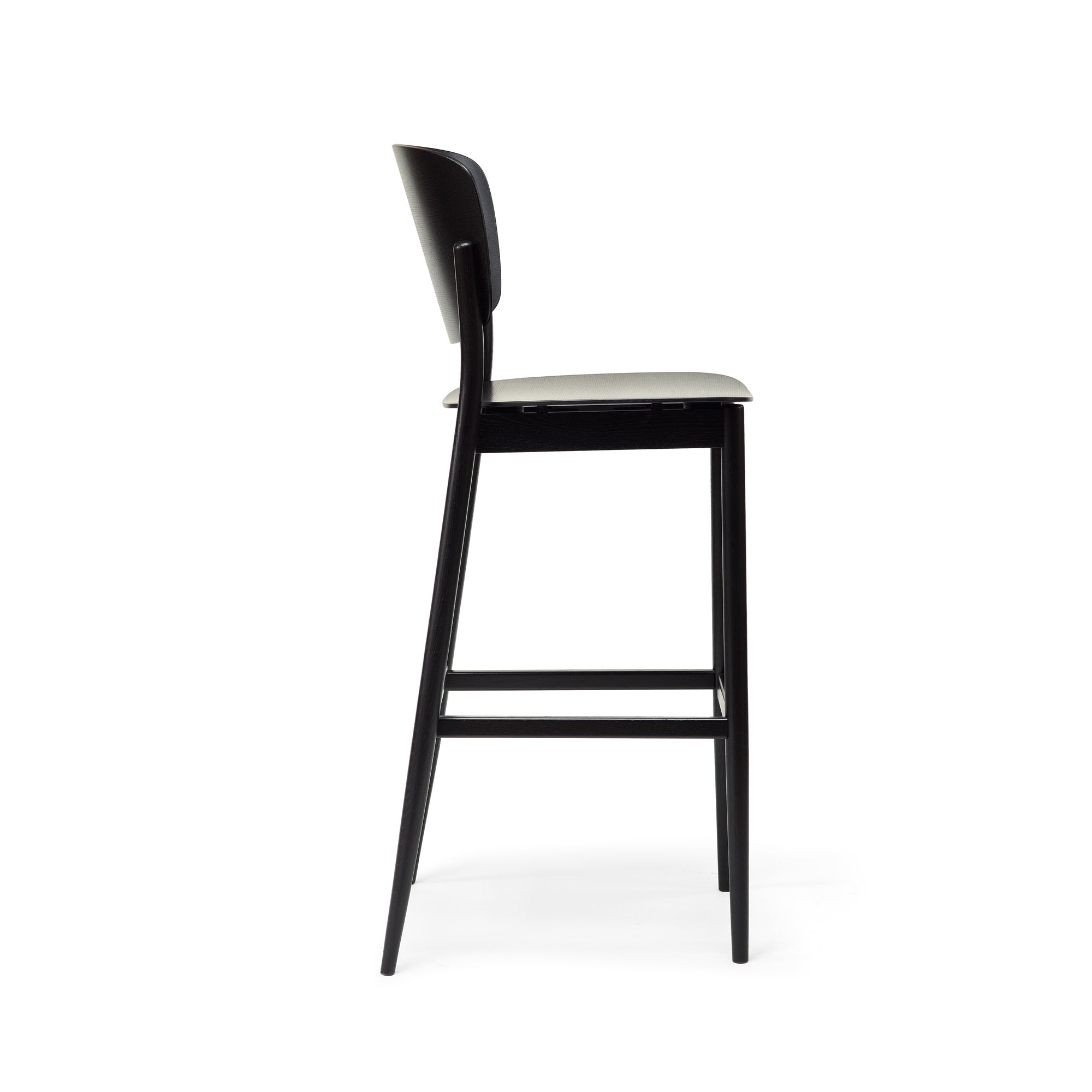The Barstool Valencia by TON boasts a minimalist black frame and wooden seat, viewed side-on. It combines contemporary style with functionality, featuring a comfortable footrest and versatile height options for bar seating.