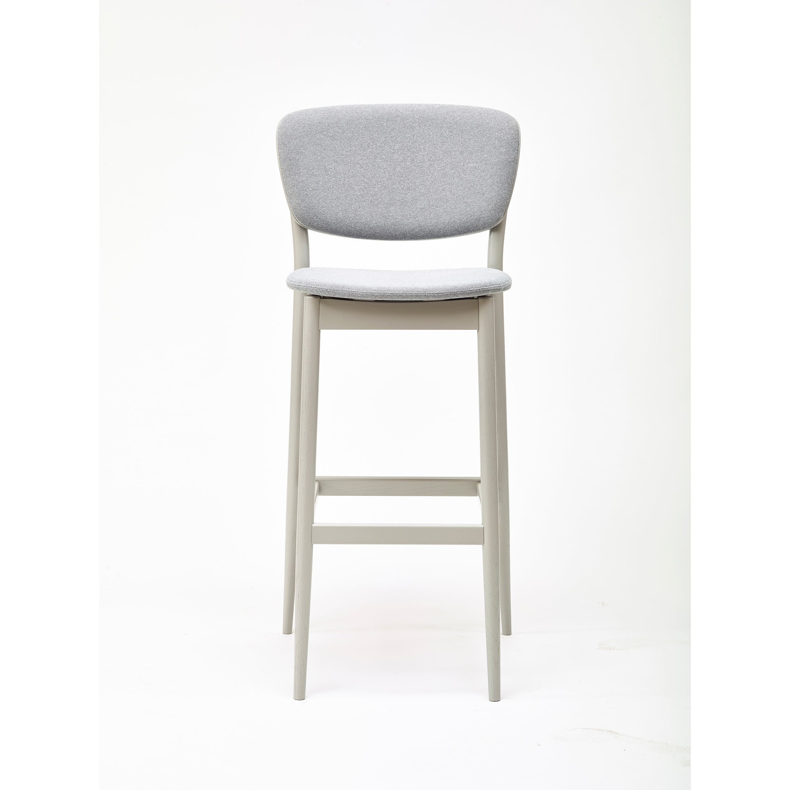 The Barstool Valencia by TON is a modern high barstool with a gray cushioned seat and backrest. Designed by Yonoh, it features sleek light wooden legs and a footrest, elegantly set against a plain white background.