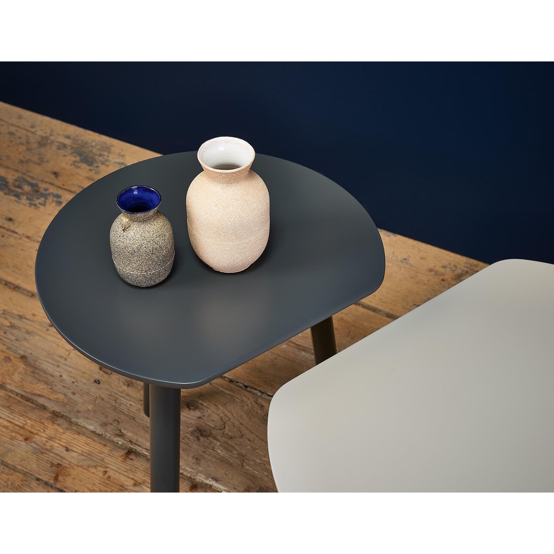 A beige ceramic vase and a gray one with a blue rim are on a dark gray table. A TON YYY Coffee Table in natural oak is partially visible on the wooden floor, against a dark blue wall.