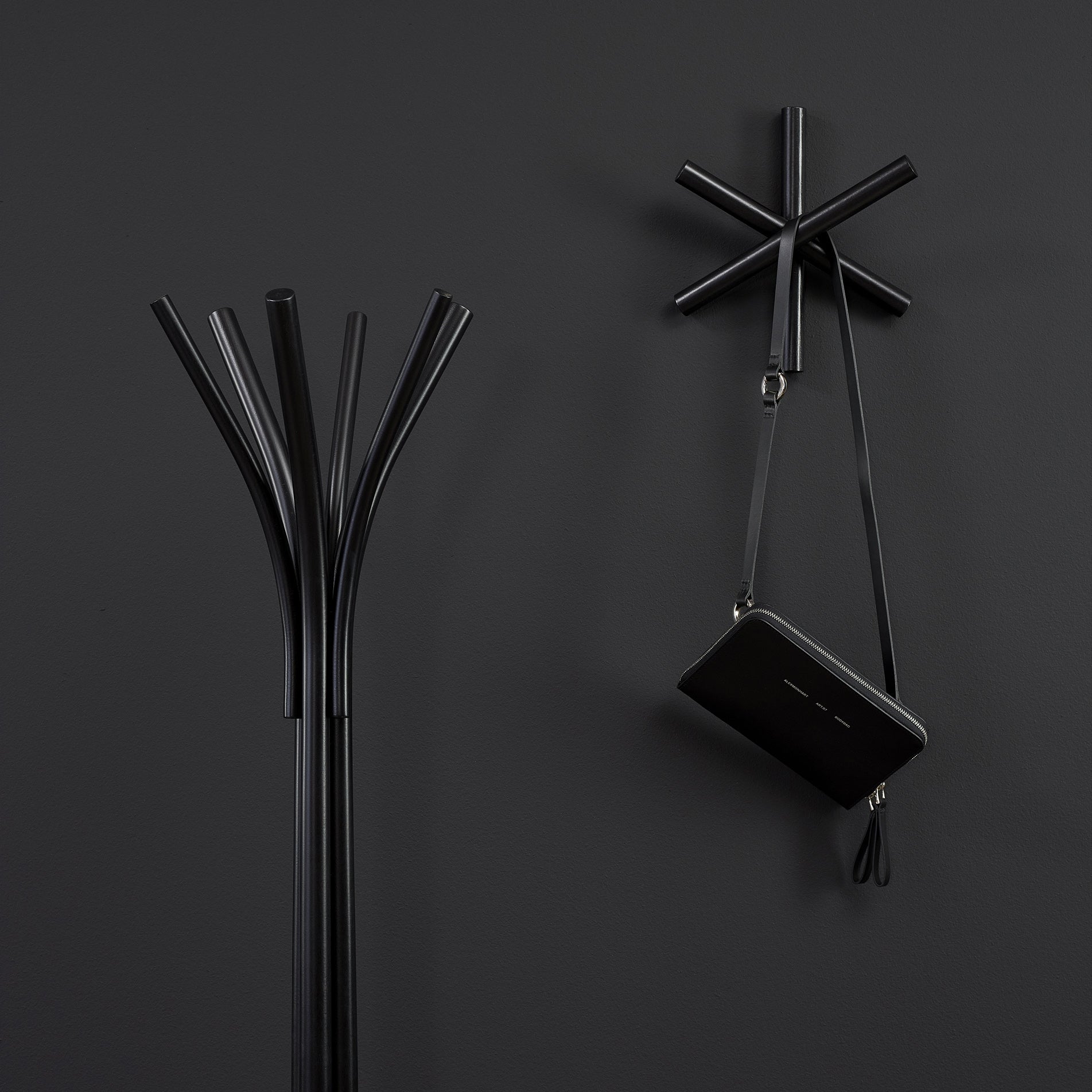 The Logs collection by TON features a black coat stand and wall-mounted rack crafted from quality wood offcuts, with abstract angular shapes and a handbag. Set against a dark gray wall, these minimalist pieces are ideal for the modern HelpSoul workspace.