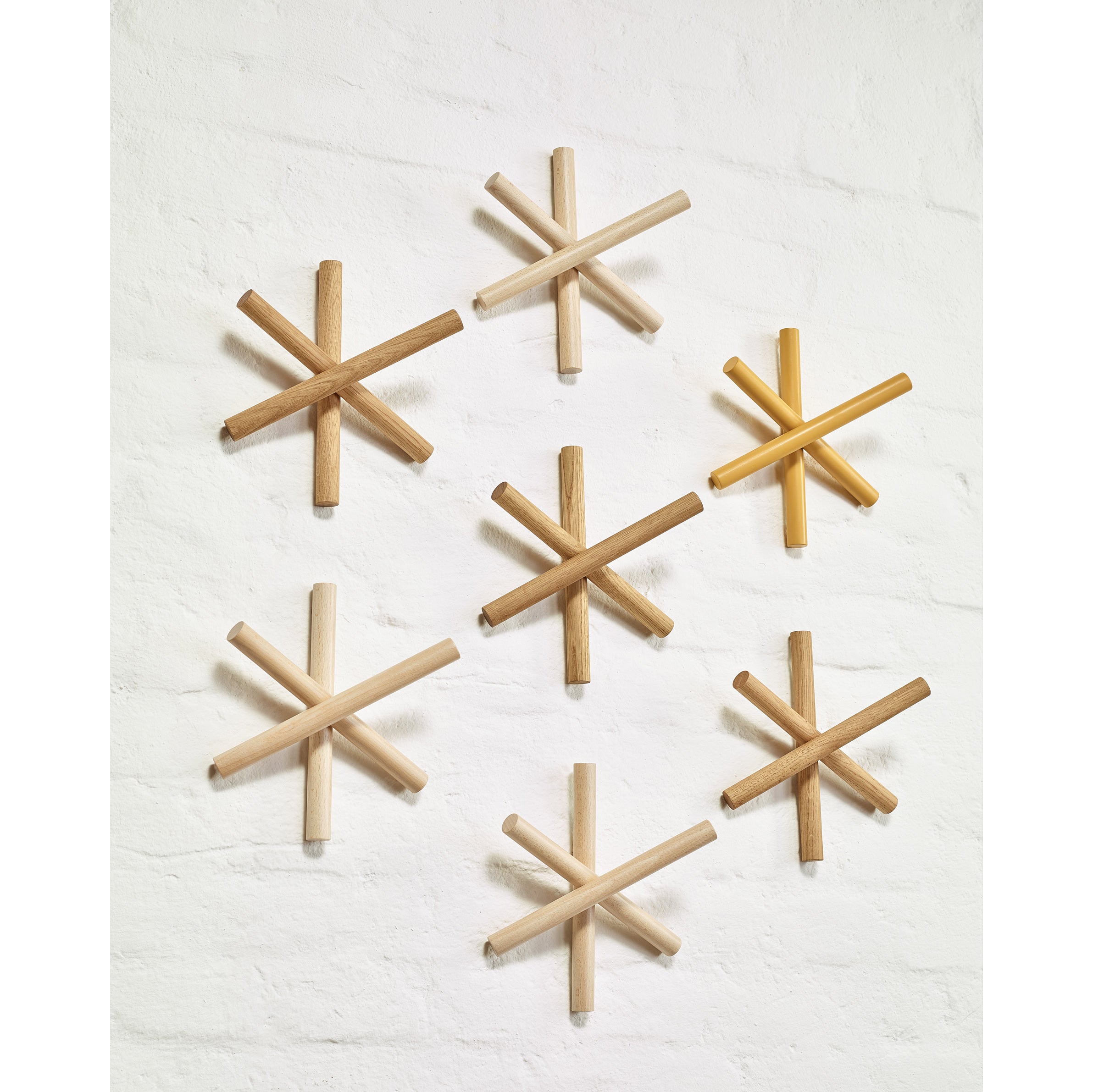 Seven Logs sculptures by TON, made from quality wood offcuts, adorn a white brick wall in the HelpSoul workspace. These interlocking cylindrical rods vary in color and size, creating an artful and balanced aesthetic with their asterisk-like design.