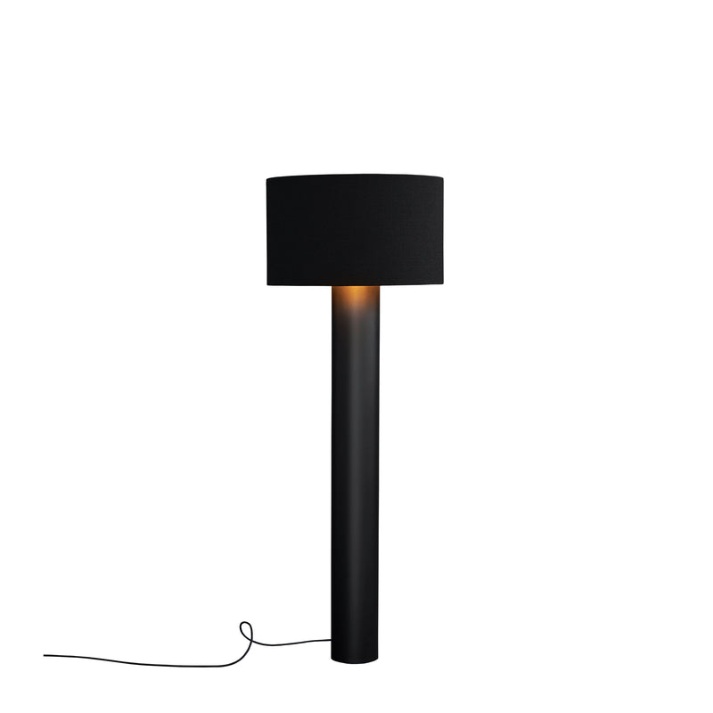 The ALL ROUND Floor Lamp by Victor Foxtrot is a modern black lamp with a cylindrical base and round wool fabric lampshade, emitting warm light. Its black power cord extends from the base, neatly laying left on a crisp white background.
