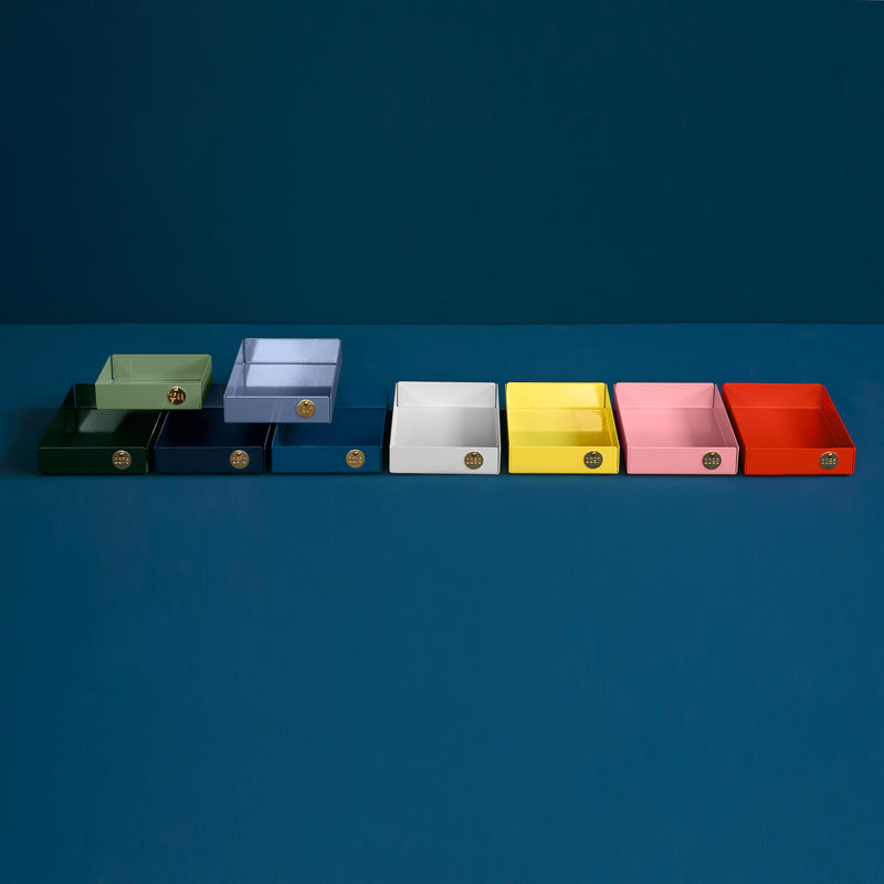 Eight POI Tray M boxes by Victor Foxtrot, crafted from powder-coated steel in green, light blue, blue, white, yellow, pink, coral, and dark green colors with a front emblem are aligned against a dark teal background. Perfect for design lovers!.