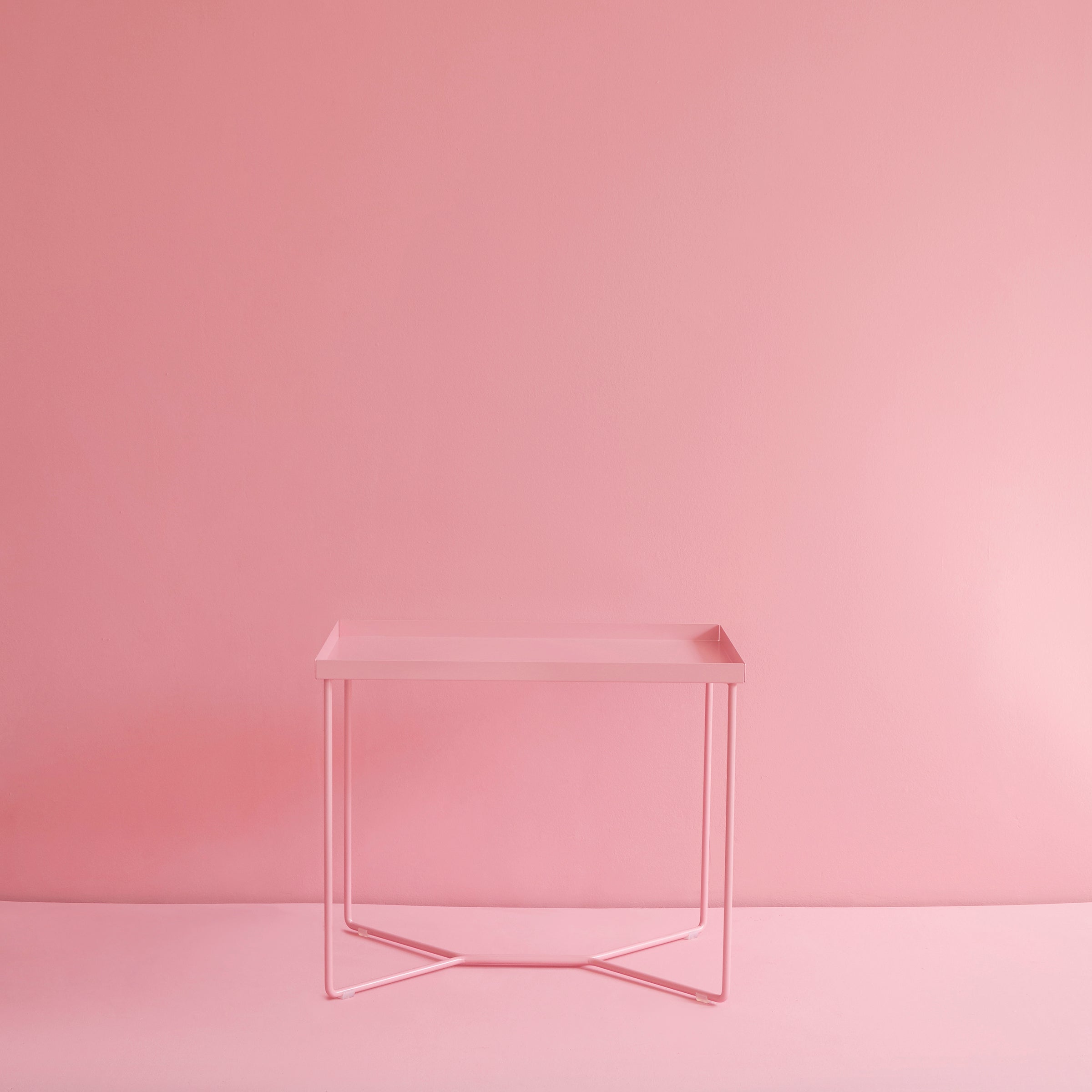 The POI SINGLE Side Table by Victor Foxtrot features a minimalist design with thin powder-coated steel legs against a matching pink background, creating a calm and cohesive monochromatic aesthetic.