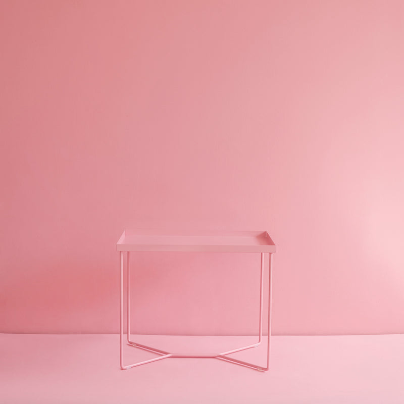The POI SINGLE Side Table by Victor Foxtrot features a minimalist design with thin powder-coated steel legs against a matching pink background, creating a calm and cohesive monochromatic aesthetic.