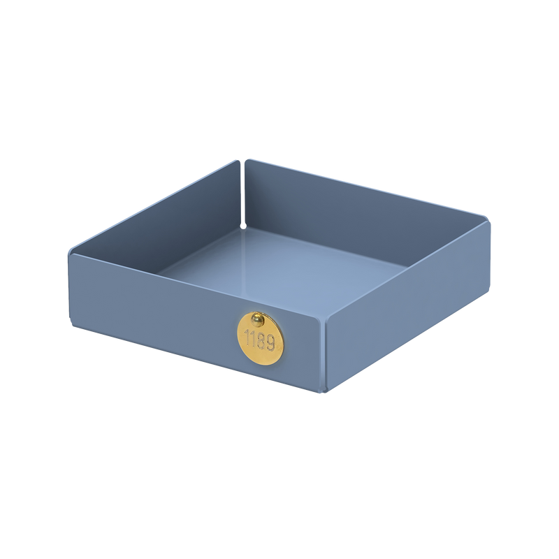 The POI Tray S by Victor Foxtrot is a square, grayish-blue powder-coated steel tray with high vertical edges and a brass label featuring 1139. Perfect for design enthusiasts, it blends form and function effortlessly against a plain white background.