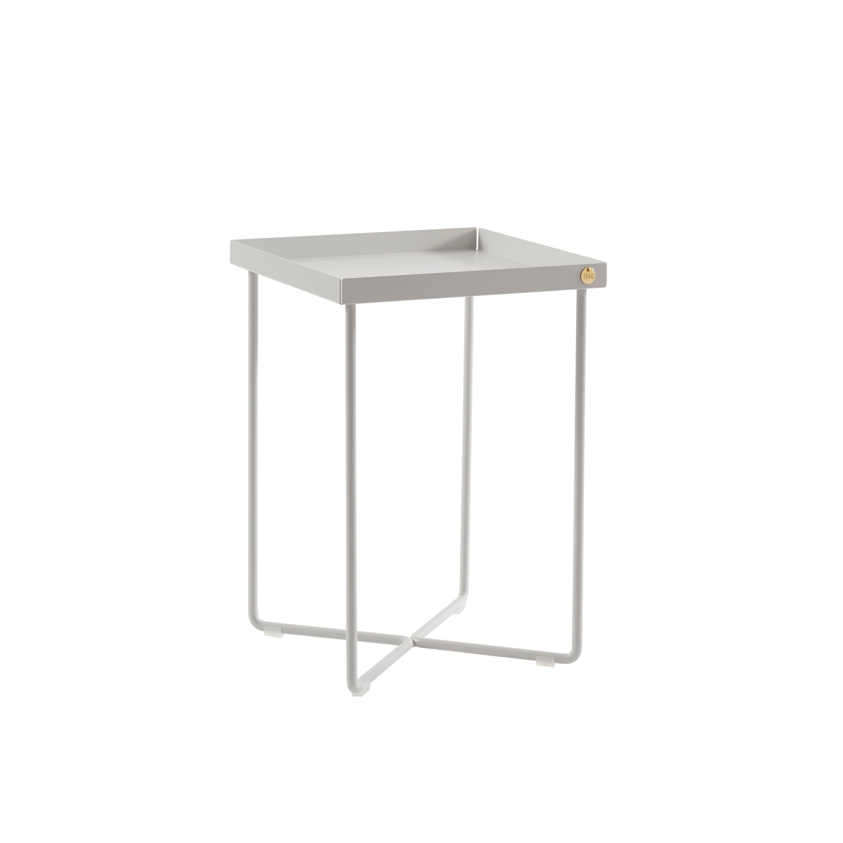 The POI MINI Side Table by Victor Foxtrot is a minimalist, square bedside table with a gray metal tray top, thin legs, a simple modern design, and a subtle gold emblem on one corner of the tray. It sits against a plain white background.