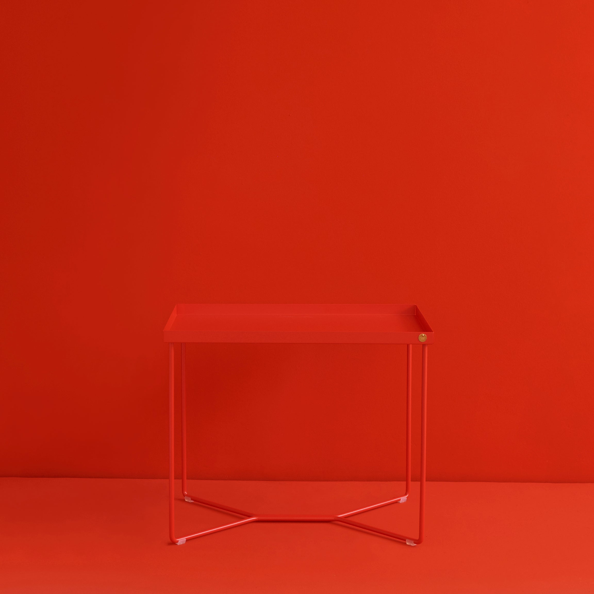 The POI SINGLE Side Table by Victor Foxtrot boasts a minimalist design, featuring a modern rectangular red top and slender powder-coated steel legs, creating an impressive monochromatic look against a seamless red background.