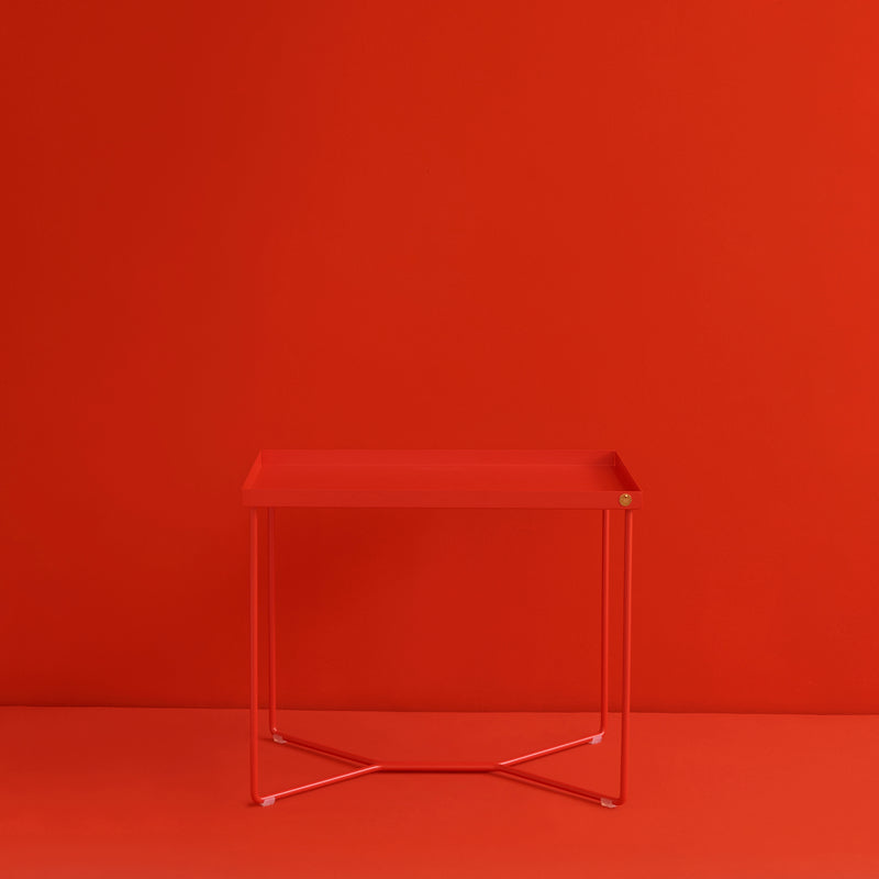 The POI SINGLE Side Table by Victor Foxtrot boasts a minimalist design, featuring a modern rectangular red top and slender powder-coated steel legs, creating an impressive monochromatic look against a seamless red background.