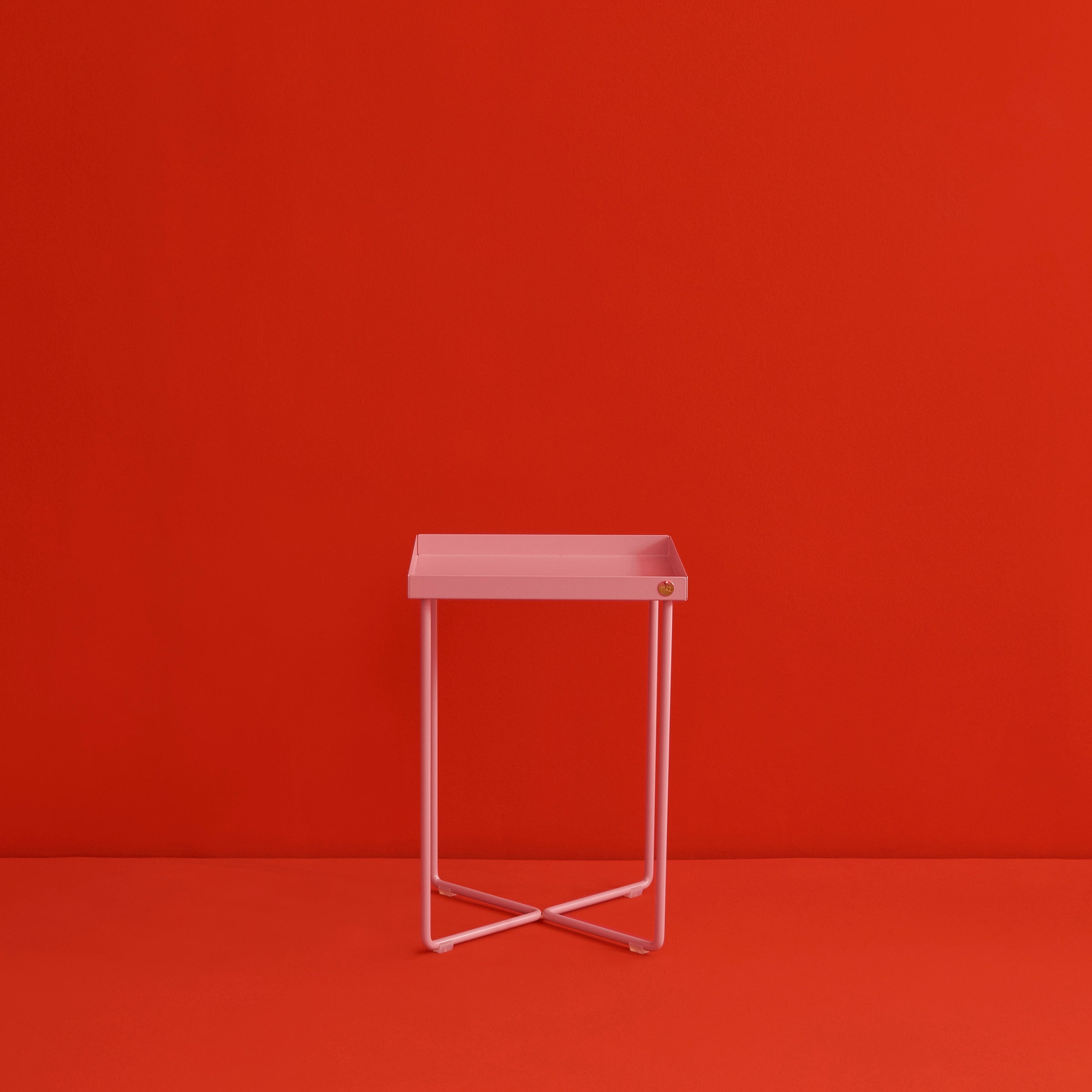 The POI MINI Side Table by Victor Foxtrot, with its minimalist pink square seat and thin metal legs, stands against a vivid red background. Its modern design and small corner accent enhance the striking color contrast, resembling a sleek mini table.
