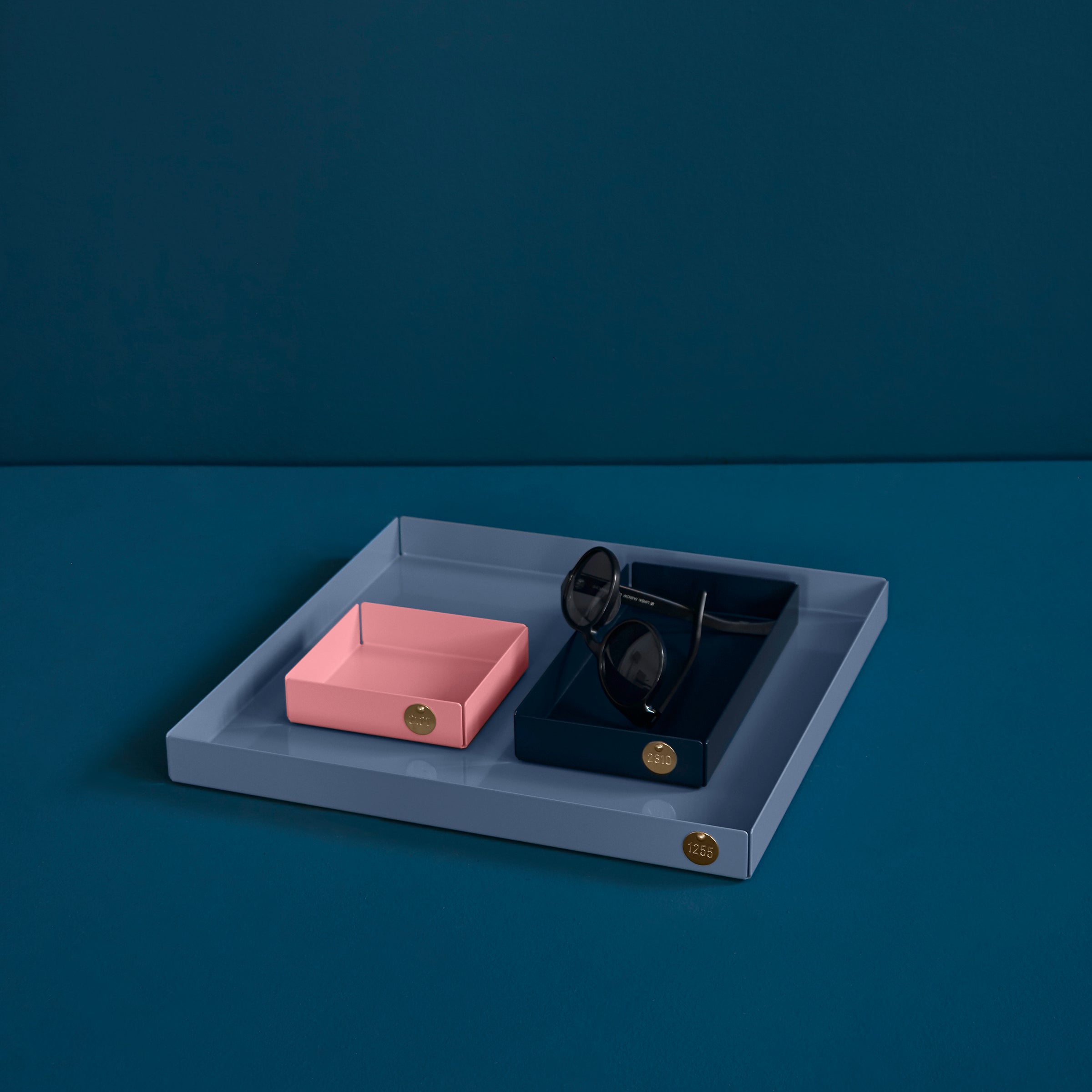 Victor Foxtrots POI Tray S - Sale, crafted for design lovers, showcases a square layout with distinct compartments in powder-coated steel. It features a larger navy section and smaller pink box against a deep teal backdrop, ideal for stylishly holding accessories like sunglasses.