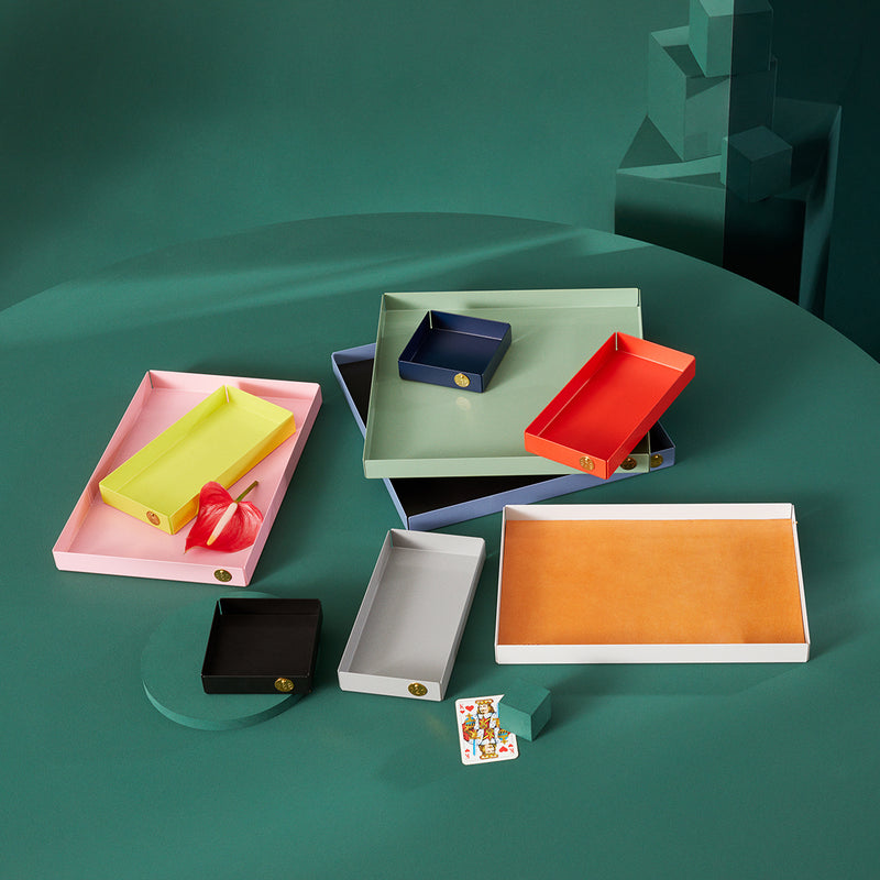 On a green surface, Victor Foxtrots vibrant POI Tray XL collection in pink, yellow, navy, green, red, and orange is artfully displayed with playing cards and a striking red flower—a perfect scene for design lovers.