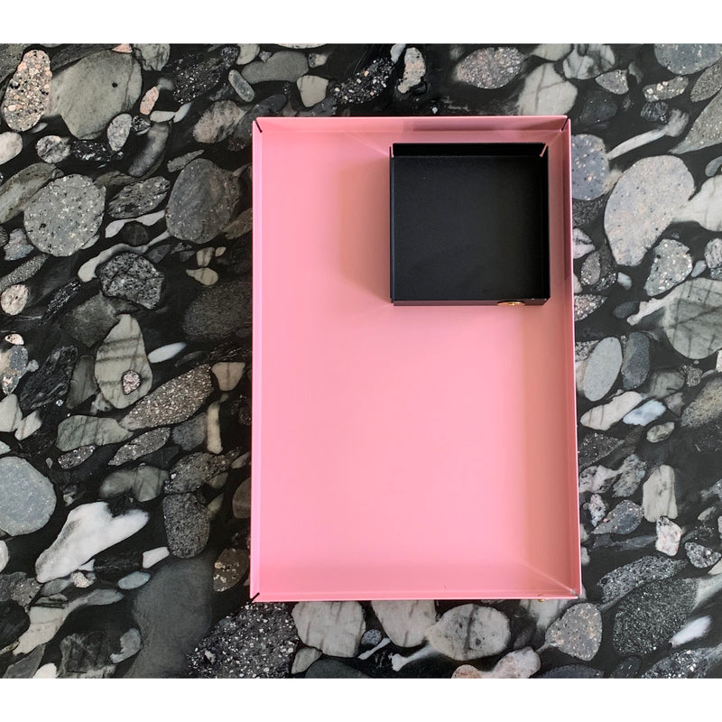 A Victor Foxtrot POI Tray L in pink holds a black square box, elegantly placed on a speckled stone-patterned surface.