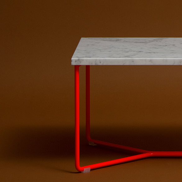 Explore the POI SINGLE MARBLE Side Table by Victor Foxtrot, showcasing a chic white marble tabletop with striking red metal legs, highlighted against a rich brown backdrop.