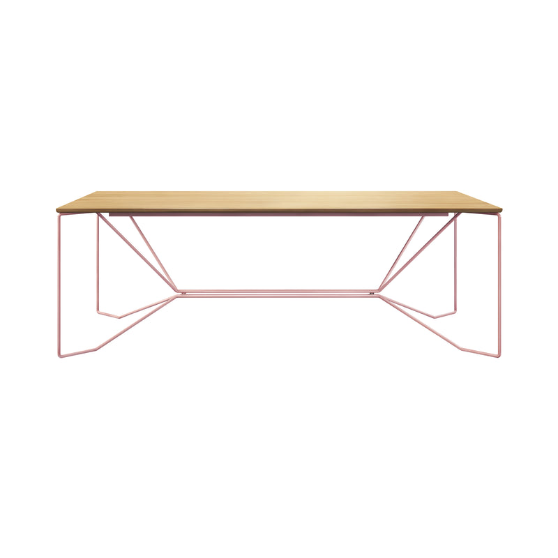 The SAME SAME Oak Table by Victor Foxtrot has a minimalist design with a solid oak top and powder-coated steel geometric pink legs, set against a white background for an open and airy look.