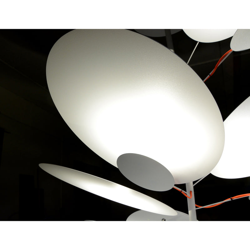 Close-up of the LEAF IT Pendant Lamp by Victor Foxtrot, showcasing modern pendant lights with overlapping round white discs that emit a soft glow in a dark room. Suspended on slim vertical rods, these lights embody an organic and minimalist design with an abstract appearance.