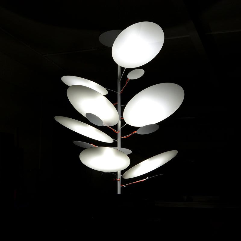 The LEAF IT Pendant Lamp by Victor Foxtrot features a modern chandelier design with circular white shades of varying sizes, resembling pendant lights on a central stem. The abstracted reflective leaves create an organic appearance against a dark background.